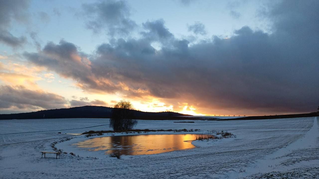 Verschneite Felder am Fuße des Katharinenbergs, die Abendsonne spiegelt sich im zugefrorenen Weiher